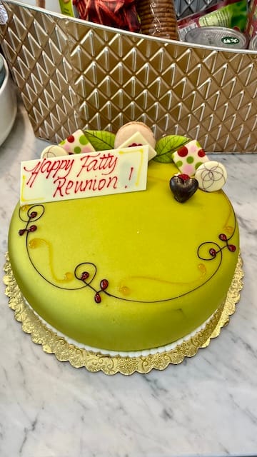 Picture of a green princess cake on a marble table. The cake has chocolate decor and says Happy Fatty Reunion in red letters.