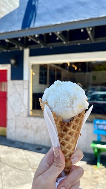 Picture of a hand holding an ice cream cone against a backdrop of the ice cream store.