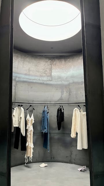 Picture of a retail store with concert walls and a skylight. Racks of clothing hang in the center.