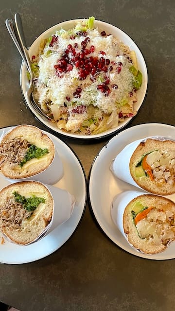 picture of a salad, roast port hoagie, and cauliflower hoagie on white plates on a table 