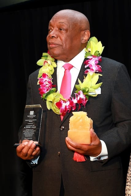 Picture of a man in a suit carrying awards in each hand