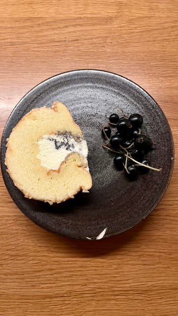 Photo of a roll cake and black currants on a black plate on a wooden table