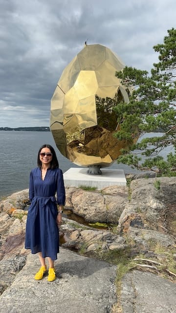 Photo of a woman standing in front of a golden egg sculpture