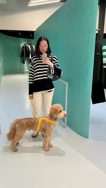 Picture of a woman in a stripped sweater and jeans and a dog in front of a turquoise wall