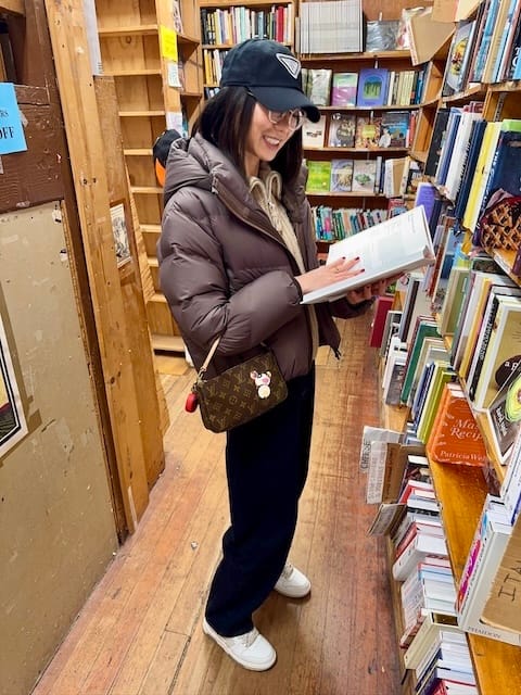 Picture of a woman in a brown jacket and black jeans looking at a book in a bookstore