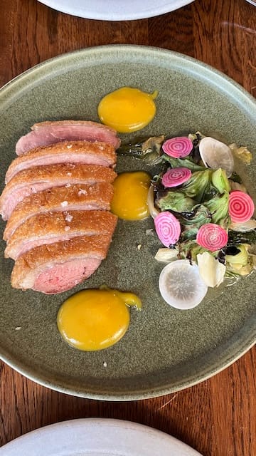 Picture of a plate of duck breast with orange sauce and a side of greens