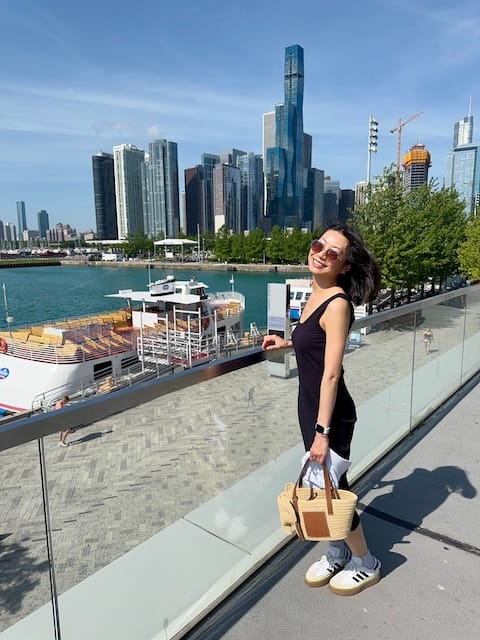 Picture of a woman wearing a navy blue dress standing in front of a pier and buildings in the background