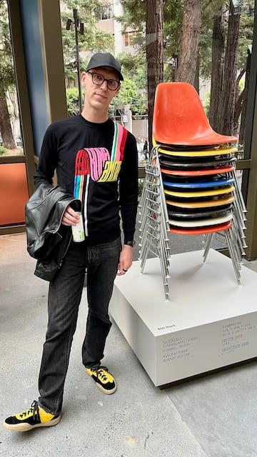 Picture of a man dressed in back next to a stack of colorful chairs