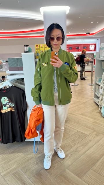 Picture of a woman in front of a mirror wearing a green jacket and white pants and shoes.