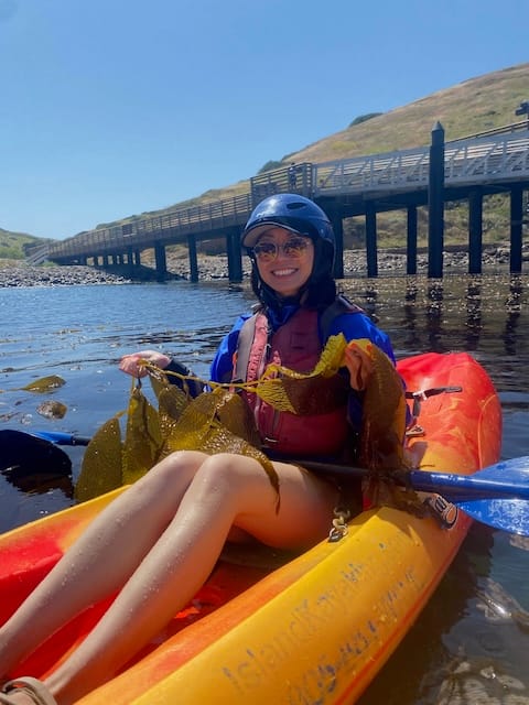 Picture of a woman on a kayak holding kelp in her hands