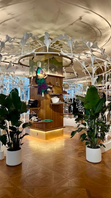 Picture of a clothing store with a cage made of calla lily sculptures surrounded by plants