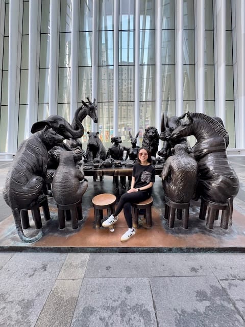 Picture of a woman sitting next to a sculpture of animals gathered at a table