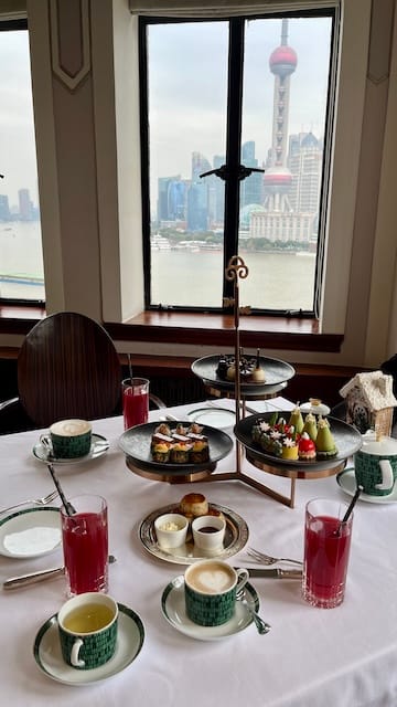 A picture of an afternoon tea set on a table with the view of the Bund in the background